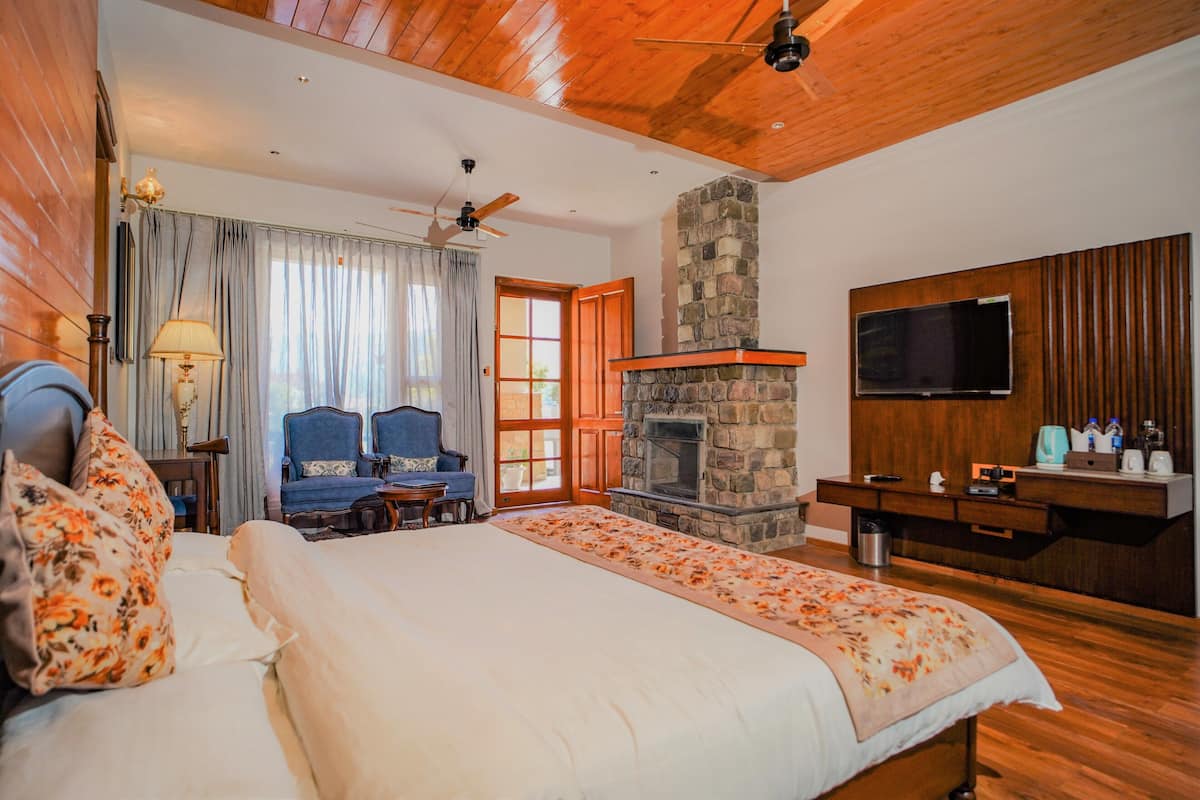 A bedroom with a bed, a stone fireplace, a television, and a wooden ceiling.