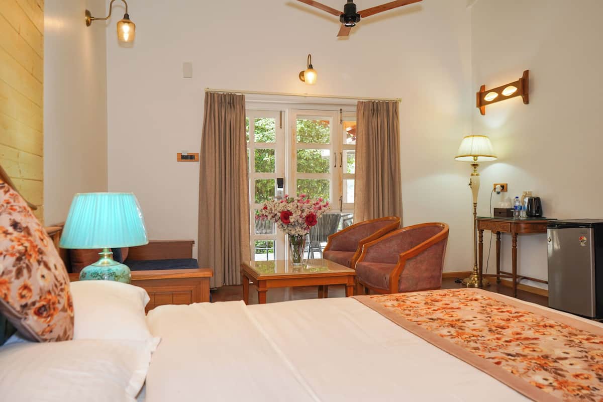 A hotel room with a bed, a desk, a chair, a lamp, a ceiling fan, and a window with curtains.