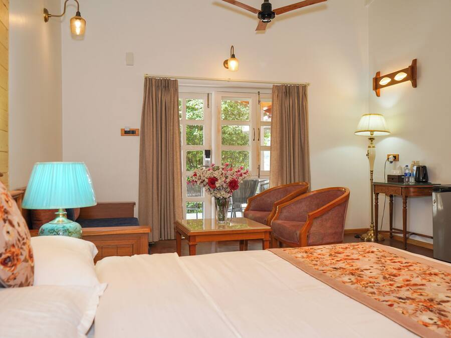 Habitación de hotel con cama, escritorio, silla, lámpara, ventilador de techo y ventana con cortinas.