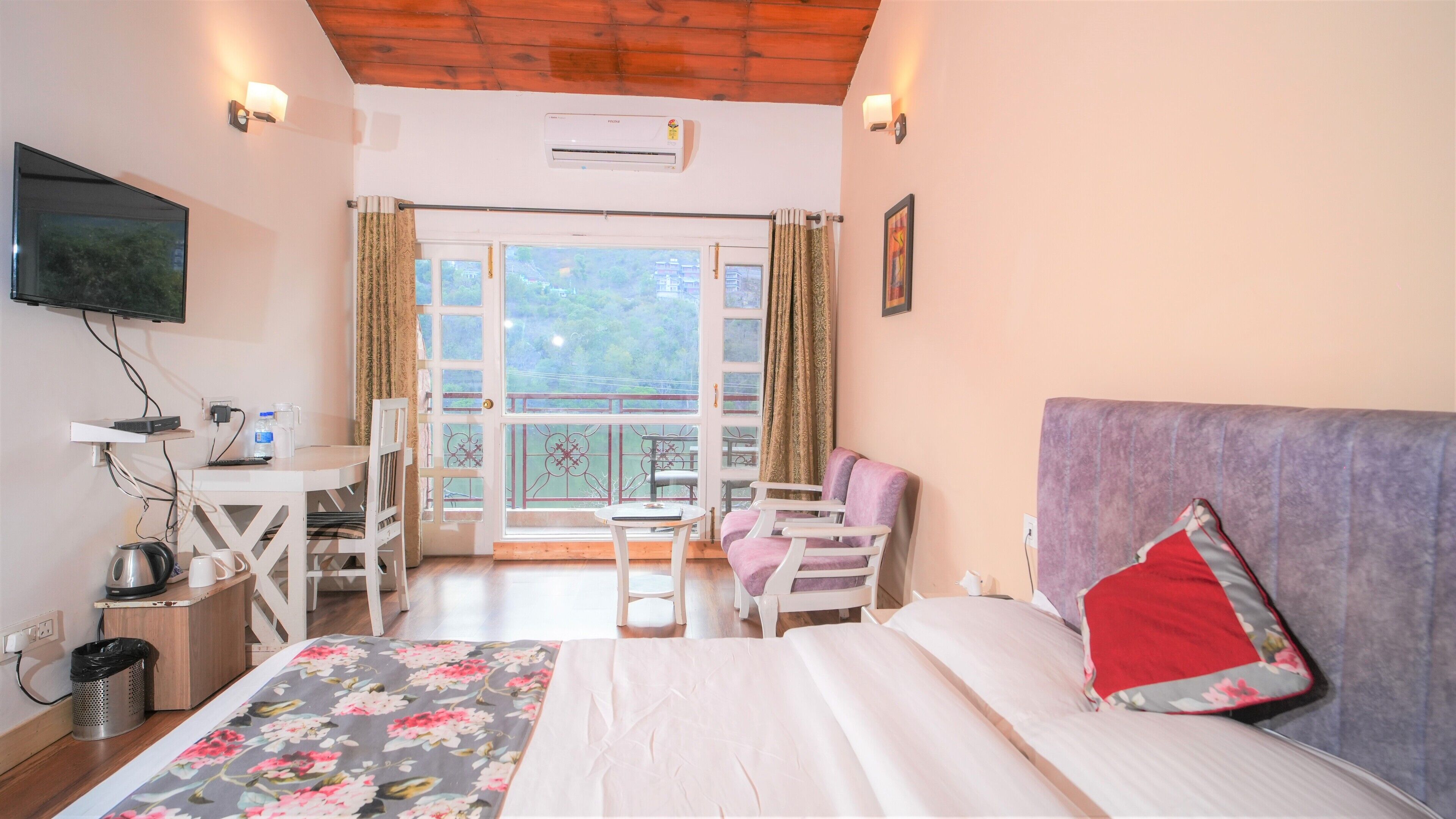 A hotel room with a bed, a desk, a chair, a TV, and a balcony with a view.
