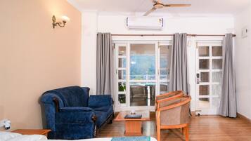 A hotel room with a bed, a blue armchair, a wooden chair, a small table, and a ceiling fan.