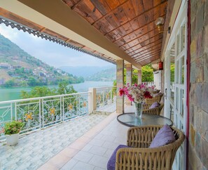 A balcony with wicker furniture, a glass table, and a vase of flowers.