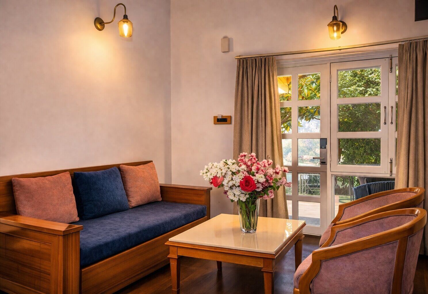 A room with a wooden sofa, a small table, and two chairs. There is a window with curtains and a view of greenery outside.