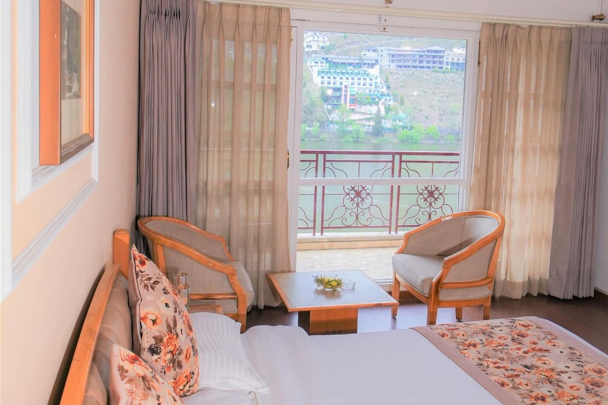 A hotel room with a bed, two chairs, a table, a window with curtains, and an air conditioning unit.