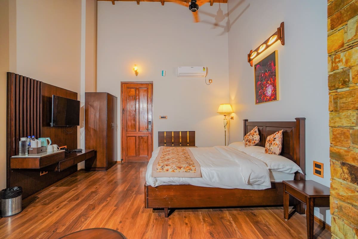A bedroom with a wooden bed, a desk with a television, a wardrobe, and a wall-mounted air conditioner.