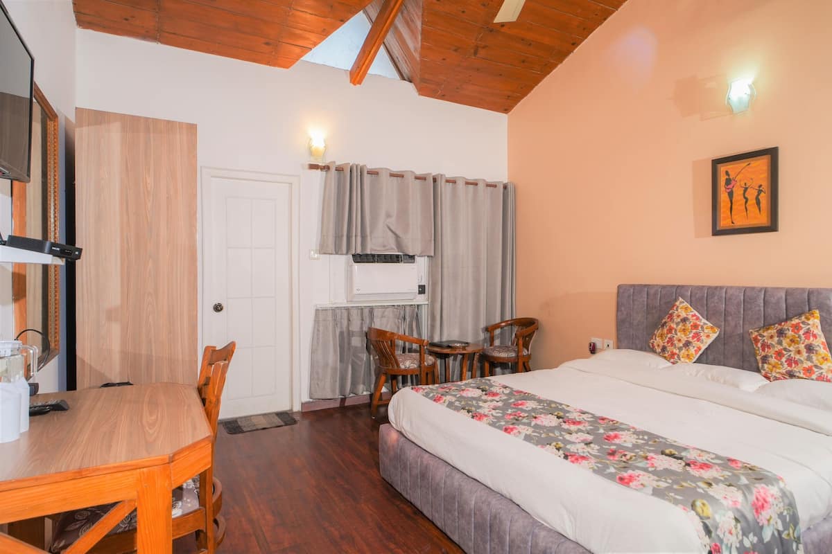 A bedroom with a bed, a desk, chairs, a window with curtains, and a wall-mounted picture.