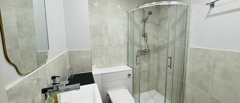 Un baño moderno con ducha de vidrio, inodoro blanco y lavamanos con dispensador de jabón.