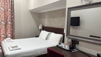 A hotel room with a neatly made bed, a bedside table with a coffee maker, a telephone, and a large mirror.