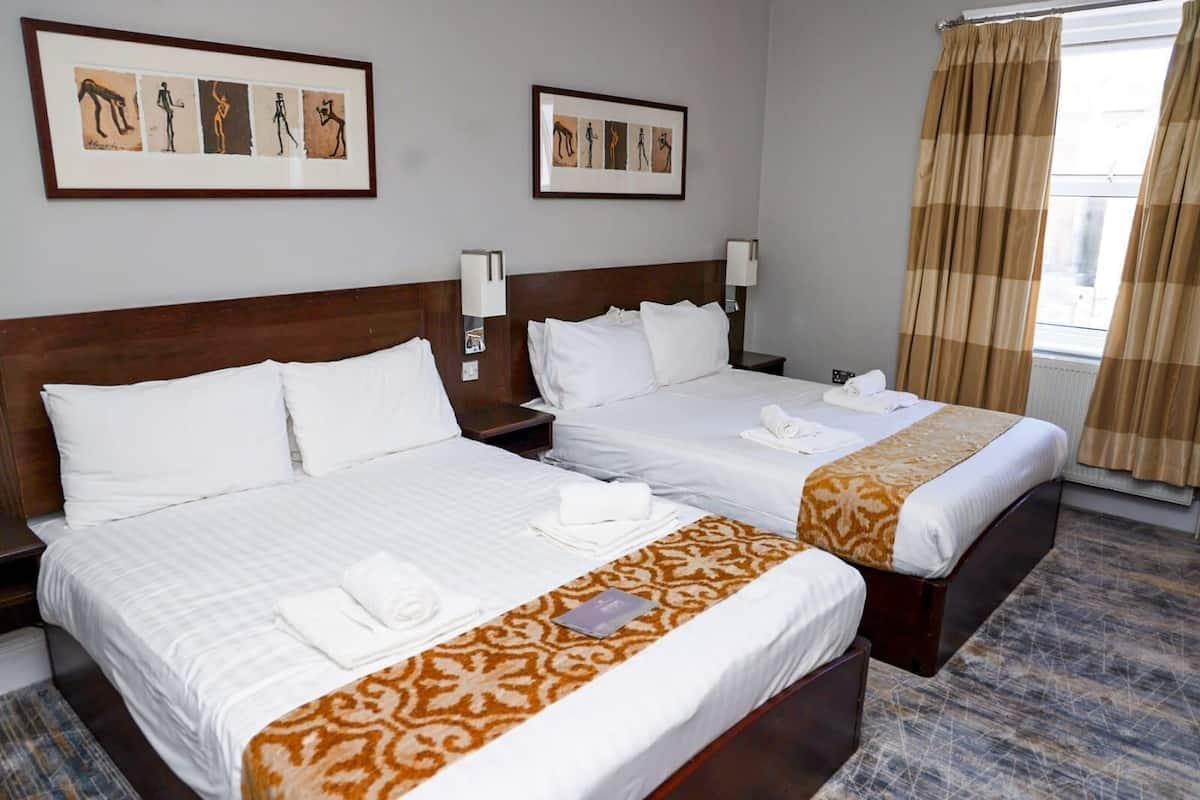 Une chambre d’hôtel avec deux lits, du linge de lit blanc, un plaid à motifs et des œuvres d’art accrochées aux murs.
