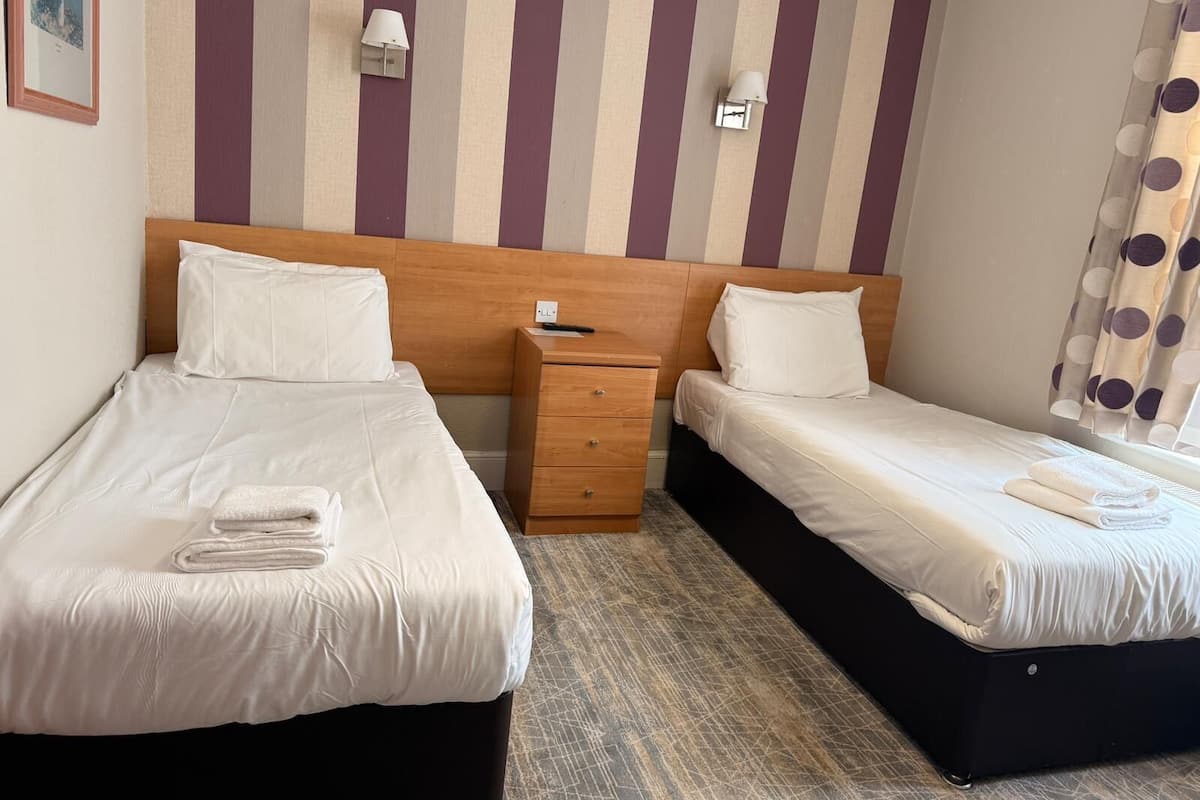 Une chambre d’hôtel avec deux lits, une tête de lit en bois, une table de chevet et un mur à rayures.
