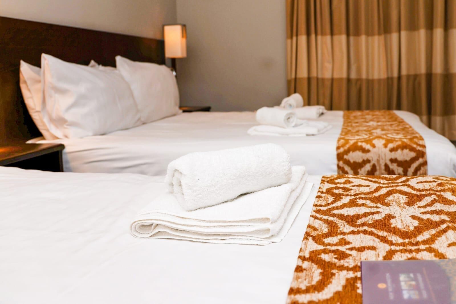 Habitación de hotel con dos camas, ropa de cama blanca y una manta marrón con estampado.