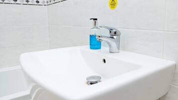 Un lavamanos blanco con grifo cromado y una botella de jabón líquido.