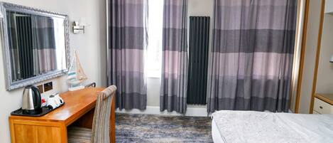 A hotel room with a bed, a desk with a chair, a mirror, and curtains.