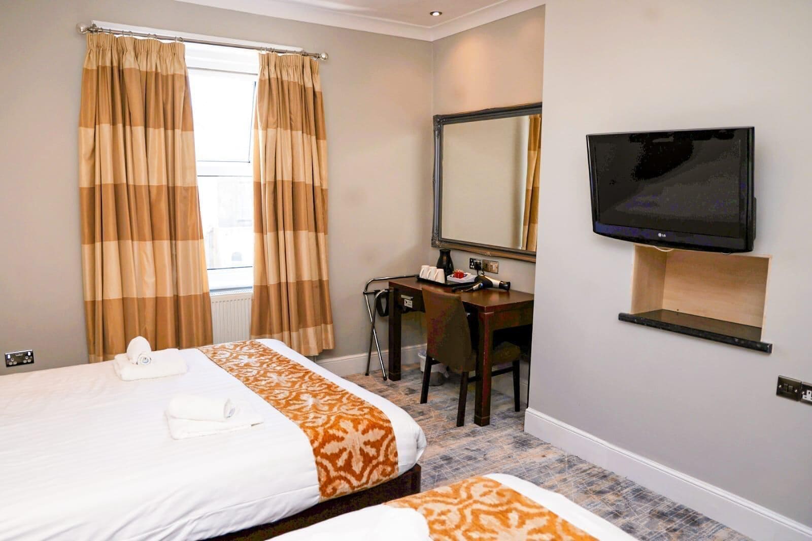 A hotel room with two beds, a desk, a chair, a television, and a large mirror.