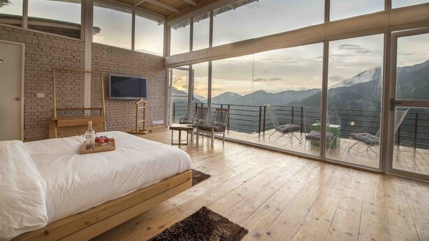 A bedroom with a large bed, a TV, and a balcony with chairs and a table. - Seclude Ramgarh, Cliff's Edge (Kosiyakutoli)