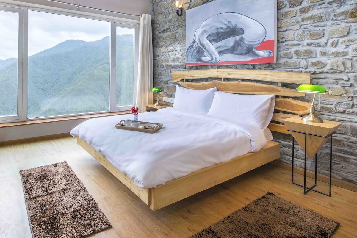 A bedroom with a wooden bed, a stone wall, a large window, and a ceiling fan.