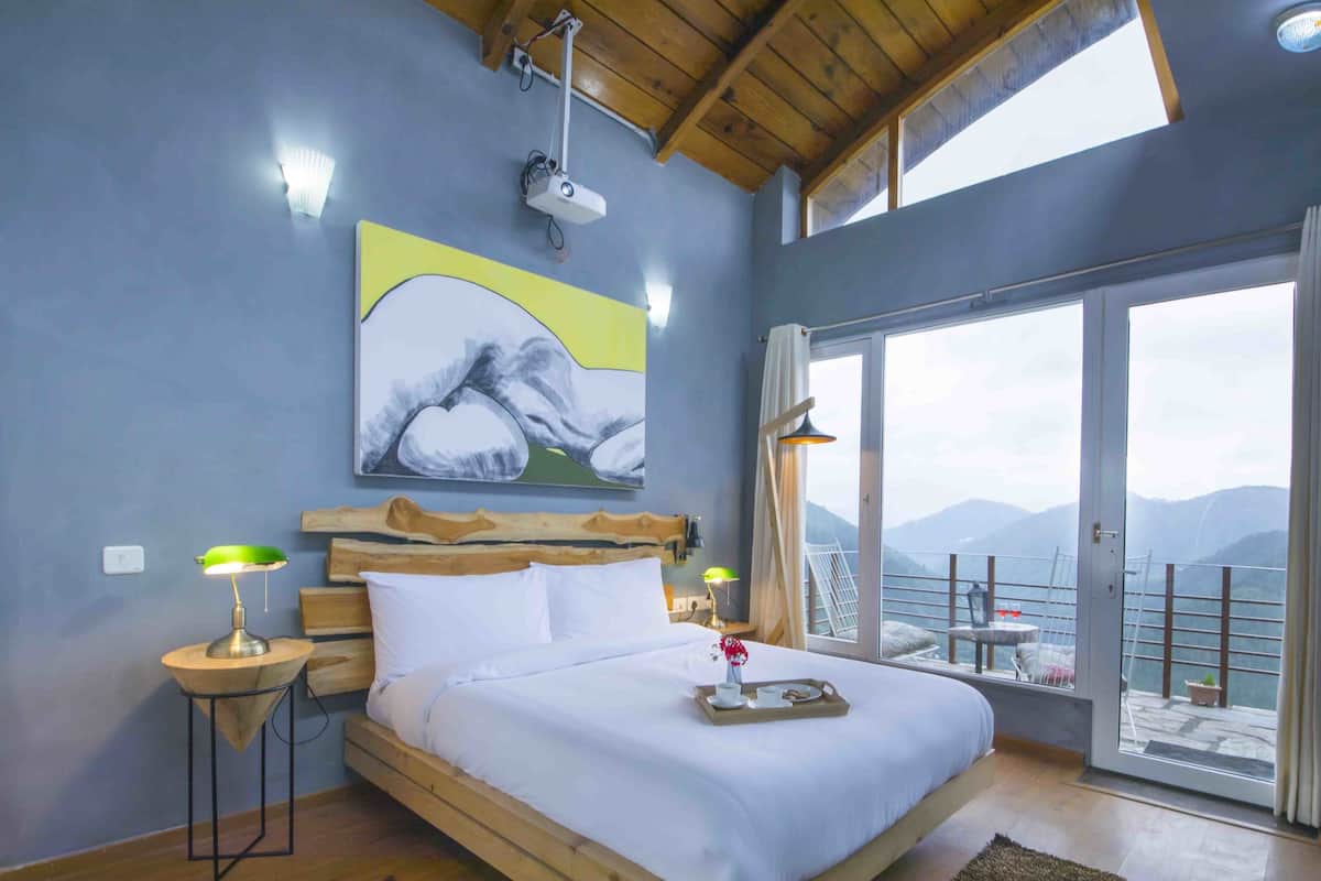 A bedroom with a large bed, wooden headboard, and a view of mountains through a sliding glass door.