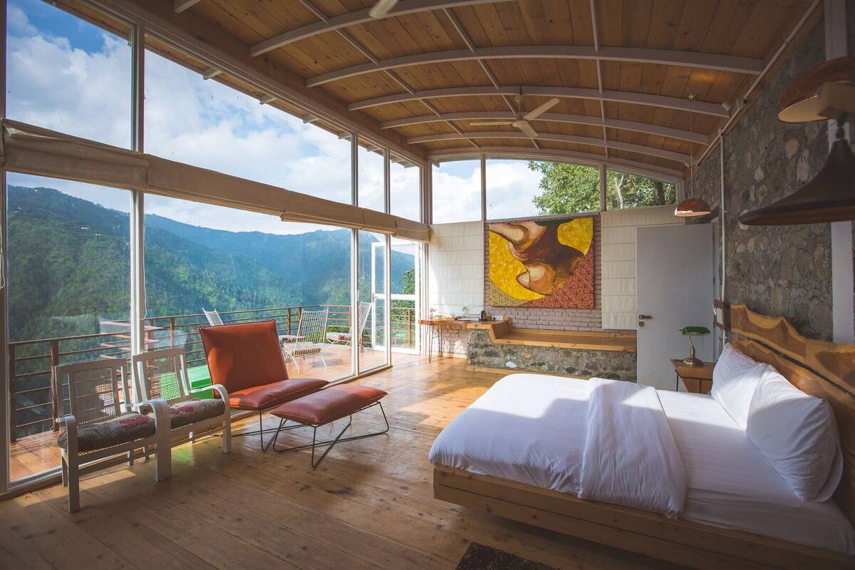 A spacious room with a large bed, a wooden ceiling, and a balcony with a view of the mountains.