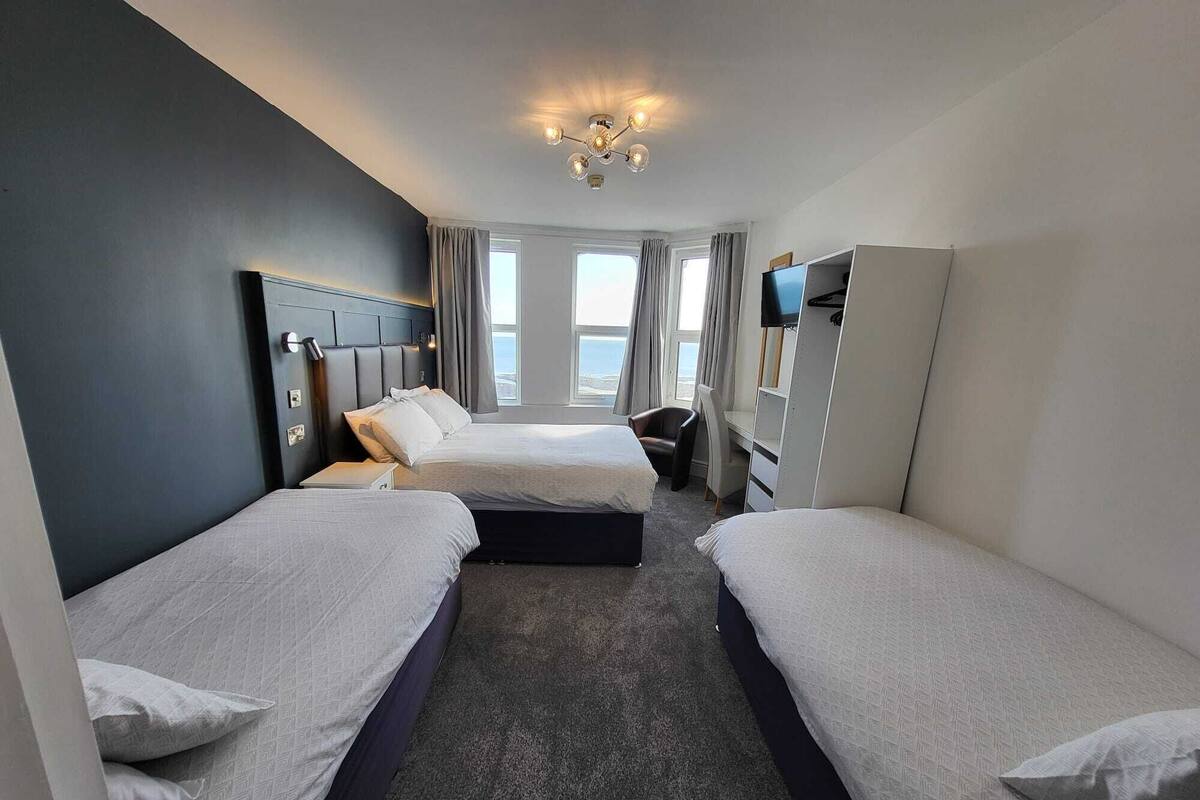 Ett hotellrum med två sängar, ett skrivbord, en stol, en TV och utsikt över havet.