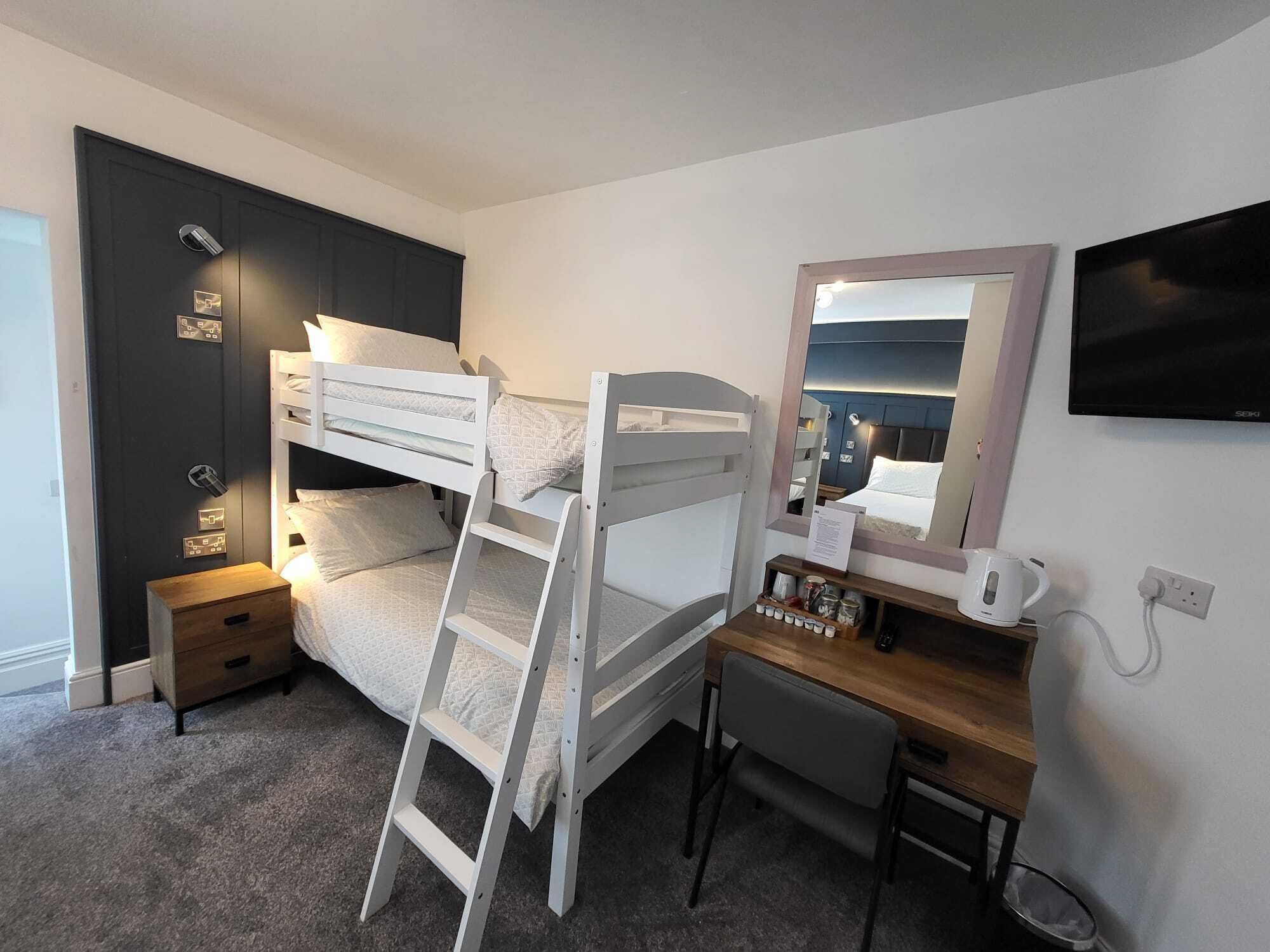 A bunk bed room with a desk, chair, and a television.