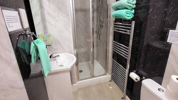 Ein modernes Badezimmer mit Duschkabine aus Glas, Waschbecken, Toilette und Handtuchhalter mit grünen Handtüchern.