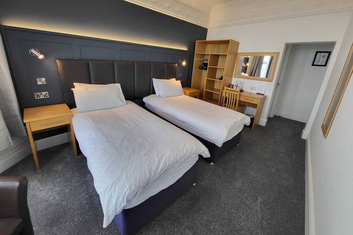 Ett hotellrum med två sängar, ett skrivbord, en garderob och en spegel.