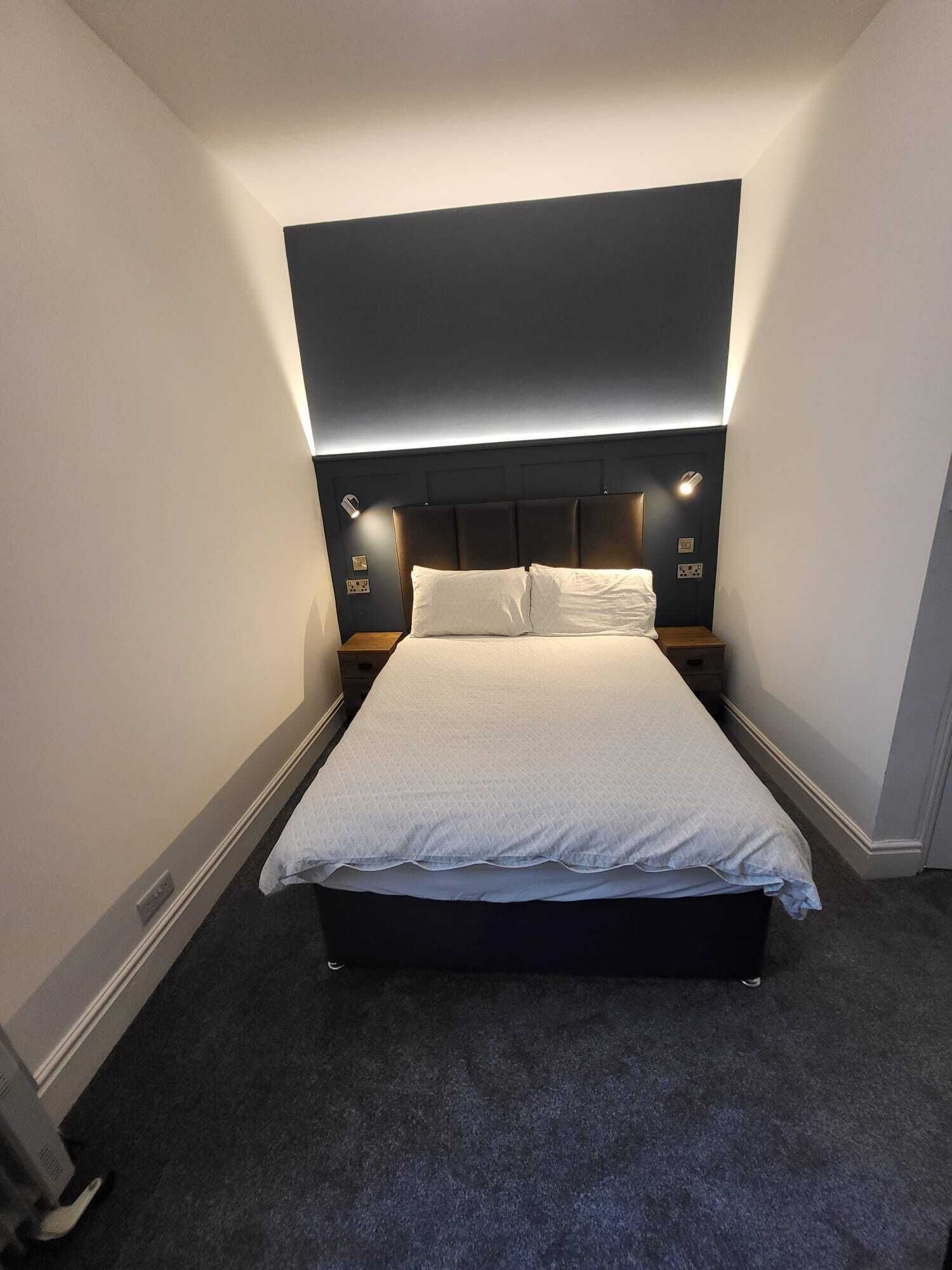 A neatly made bed in a hotel room with a dark headboard and bedside lamps.