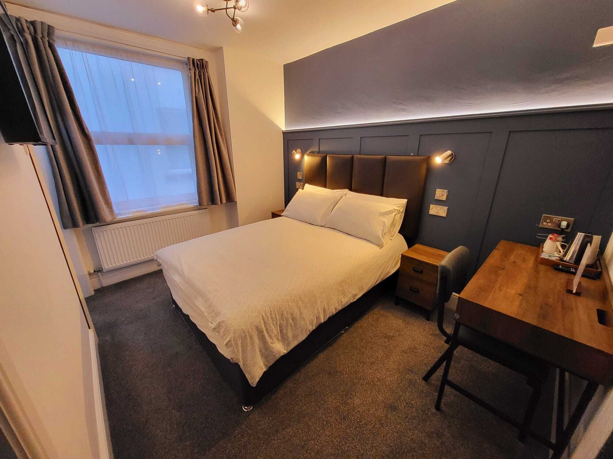 Una camera d'albergo con un letto, un comodino e una piccola scrivania.