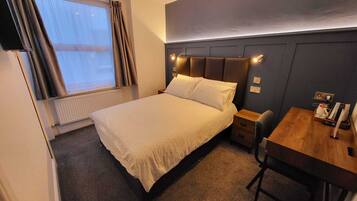 Una camera d'albergo con un letto, un comodino e una piccola scrivania.