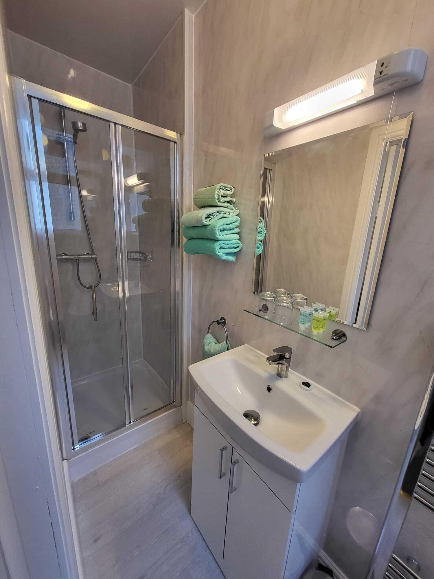 A modern bathroom with a glass shower enclosure, a white sink, and a mirror with a light above it.