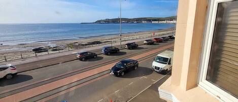 A coastal road with vehicles, a clear sky, and a distant view of the sea and hills.