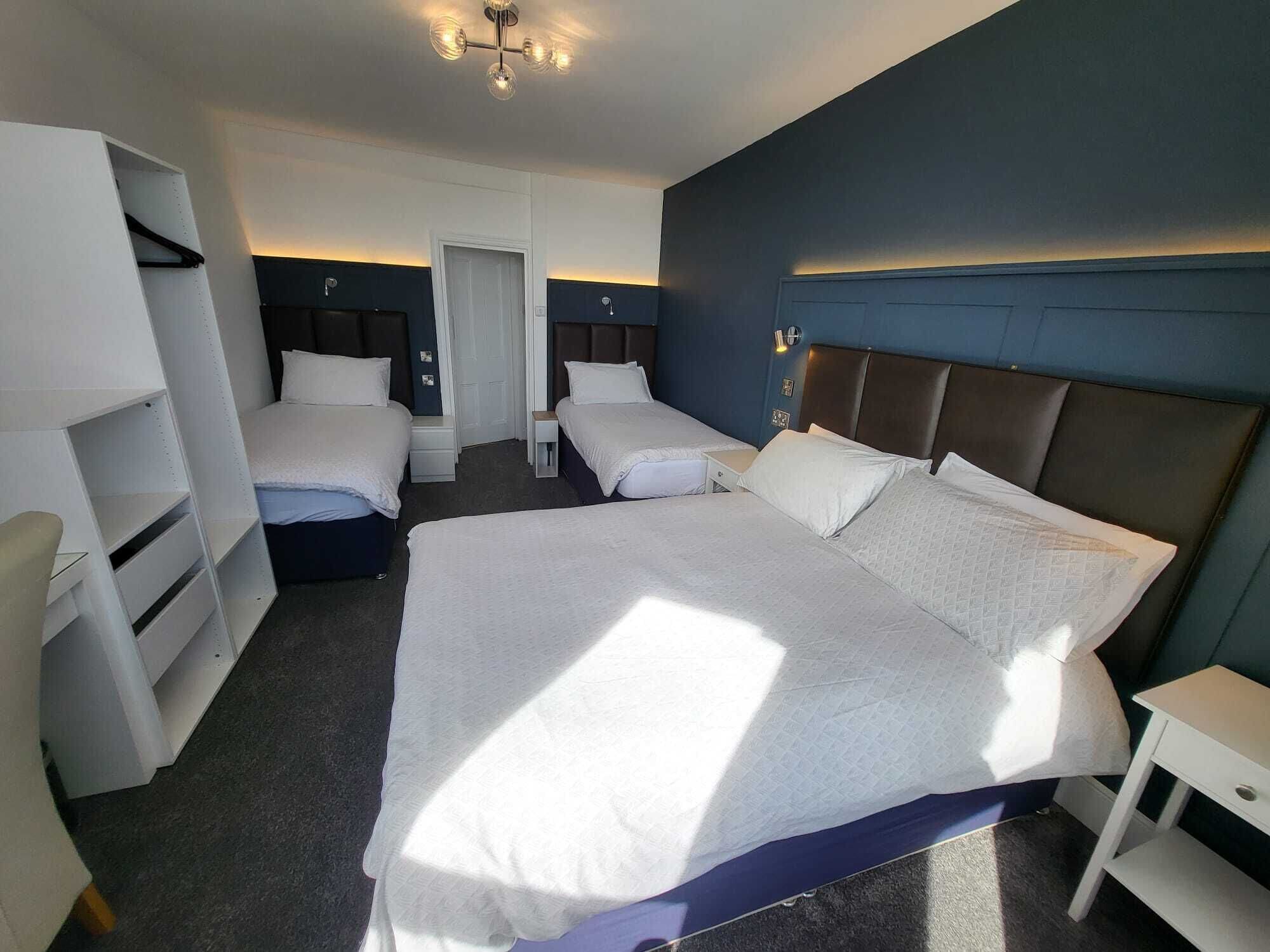 A hotel room with a large bed, two smaller beds, a wardrobe, a desk, and a chair.