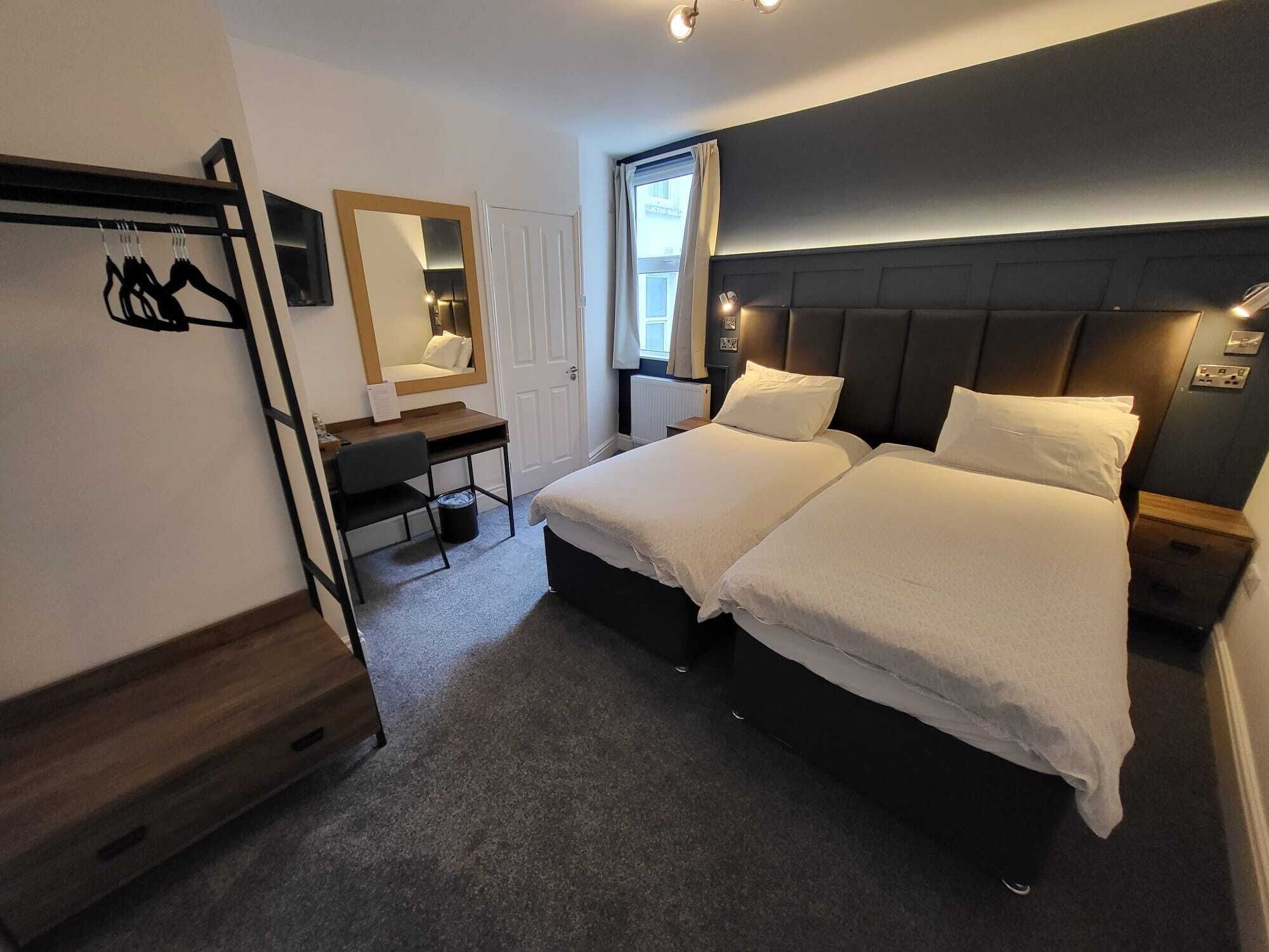 A hotel room with two beds, a desk, a chair, a mirror, and a window.