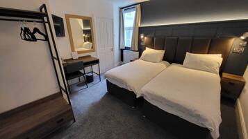 A hotel room with two beds, a desk, a chair, a mirror, and a window.