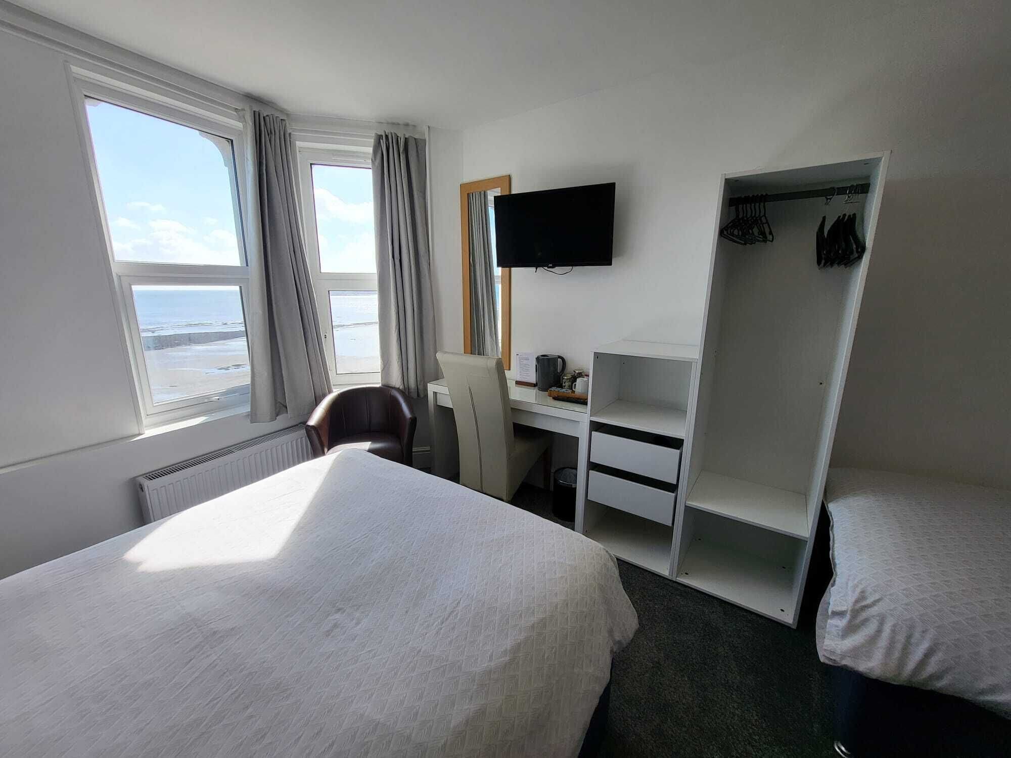 Habitación de hotel con una cama, un escritorio con silla, un televisor y un armario.