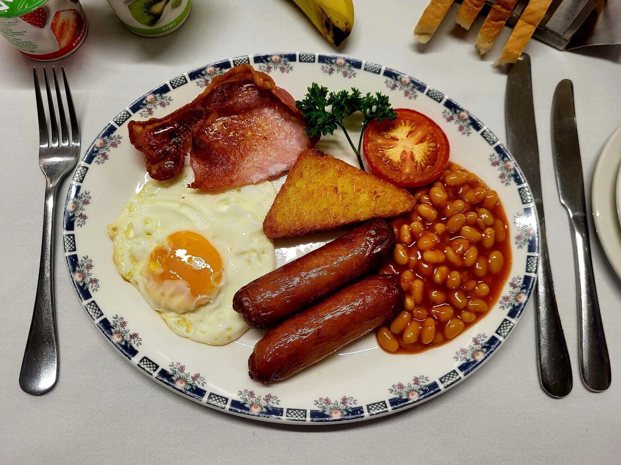 Un plato de comida para el desayuno con huevos, salchichas, tocino, tostadas, frijoles y un tomate.