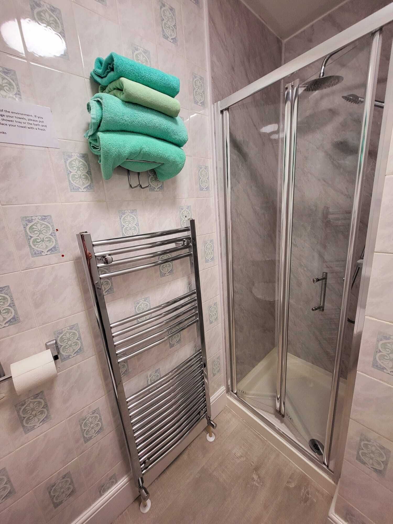 Un baño con cabina de ducha de vidrio, un perchero con toallas dobladas y un dispensador de papel higiénico.