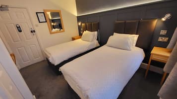 A hotel room with two single beds, a dark headboard, a bedside table, a mirror, and a door.