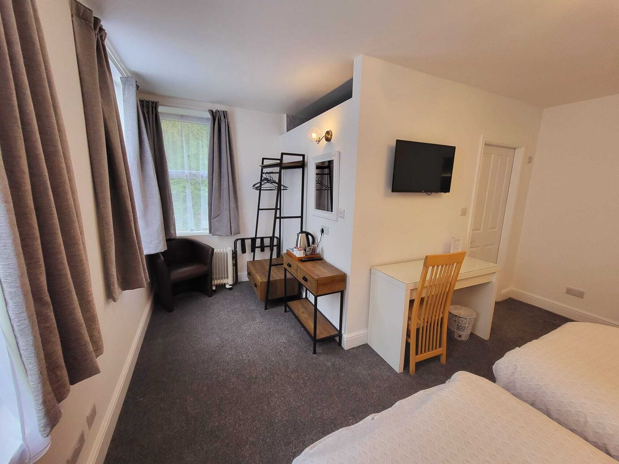 A compact hotel room with a bed, a desk, a chair, a TV, and a radiator.
