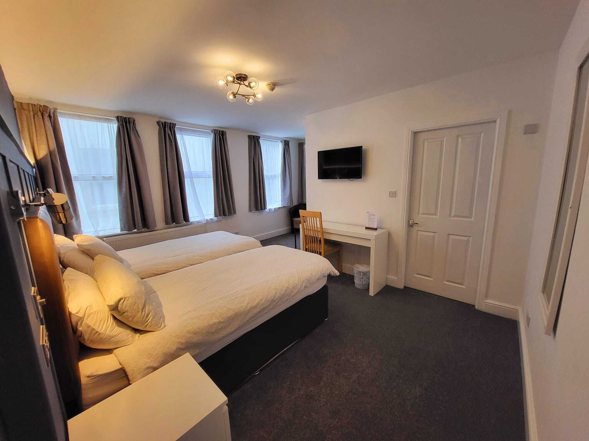 Een hotelkamer met twee bedden, een bureau, een stoel, een televisie en een deur.