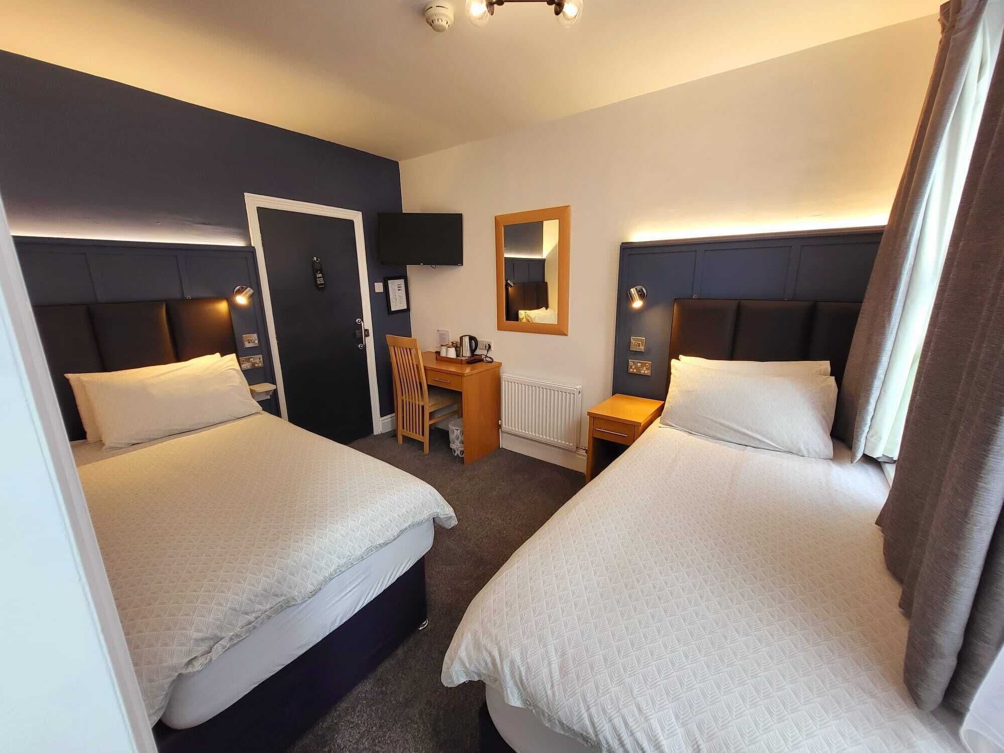 A hotel room with two beds, a desk, a chair, a TV, and a mirror.