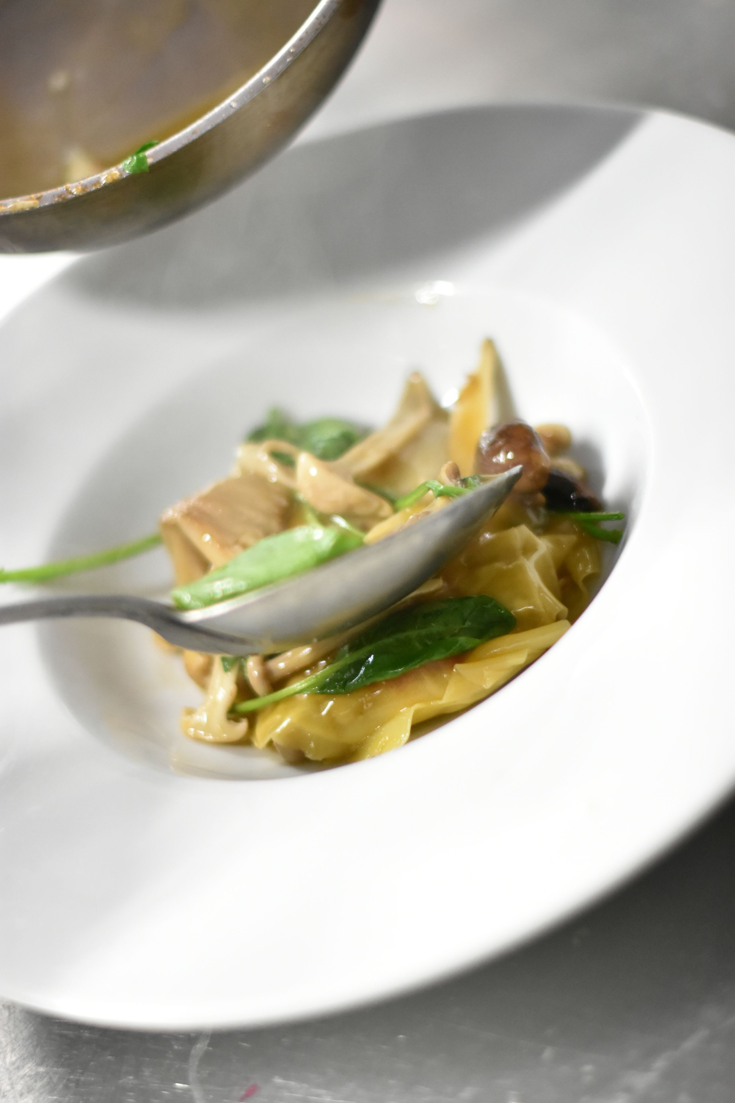 A white plate with a spoonful of noodles, green vegetables, and a piece of meat.