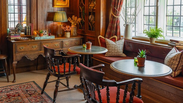 A traditional room with a wooden desk, two chairs, a round table, and a bench with cushions. - Stone House Hotel (Hawes)