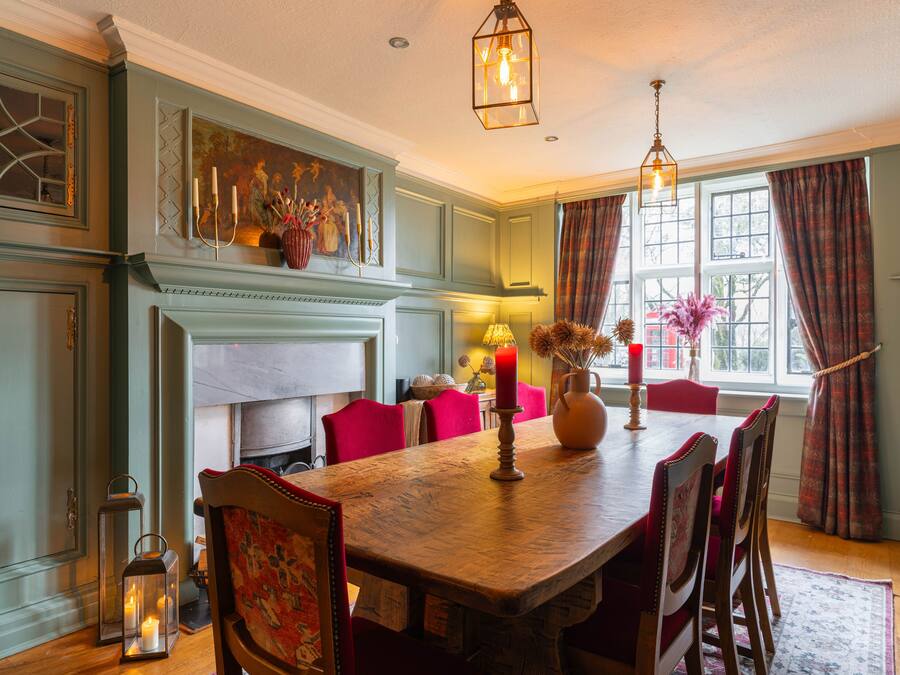 A dining room with a wooden table, red chairs, a chandelier, and a fireplace.