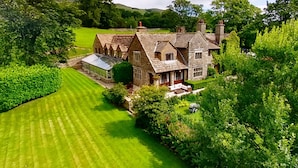 A large stone house with multiple chimneys, surrounded by lush greenery and a well-maintained lawn. - Stone House Hotel (Hawes)