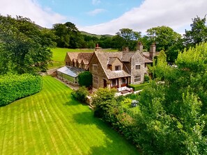 A large stone house with multiple chimneys, surrounded by lush greenery and a well-maintained lawn. - Stone House Hotel (Hawes)