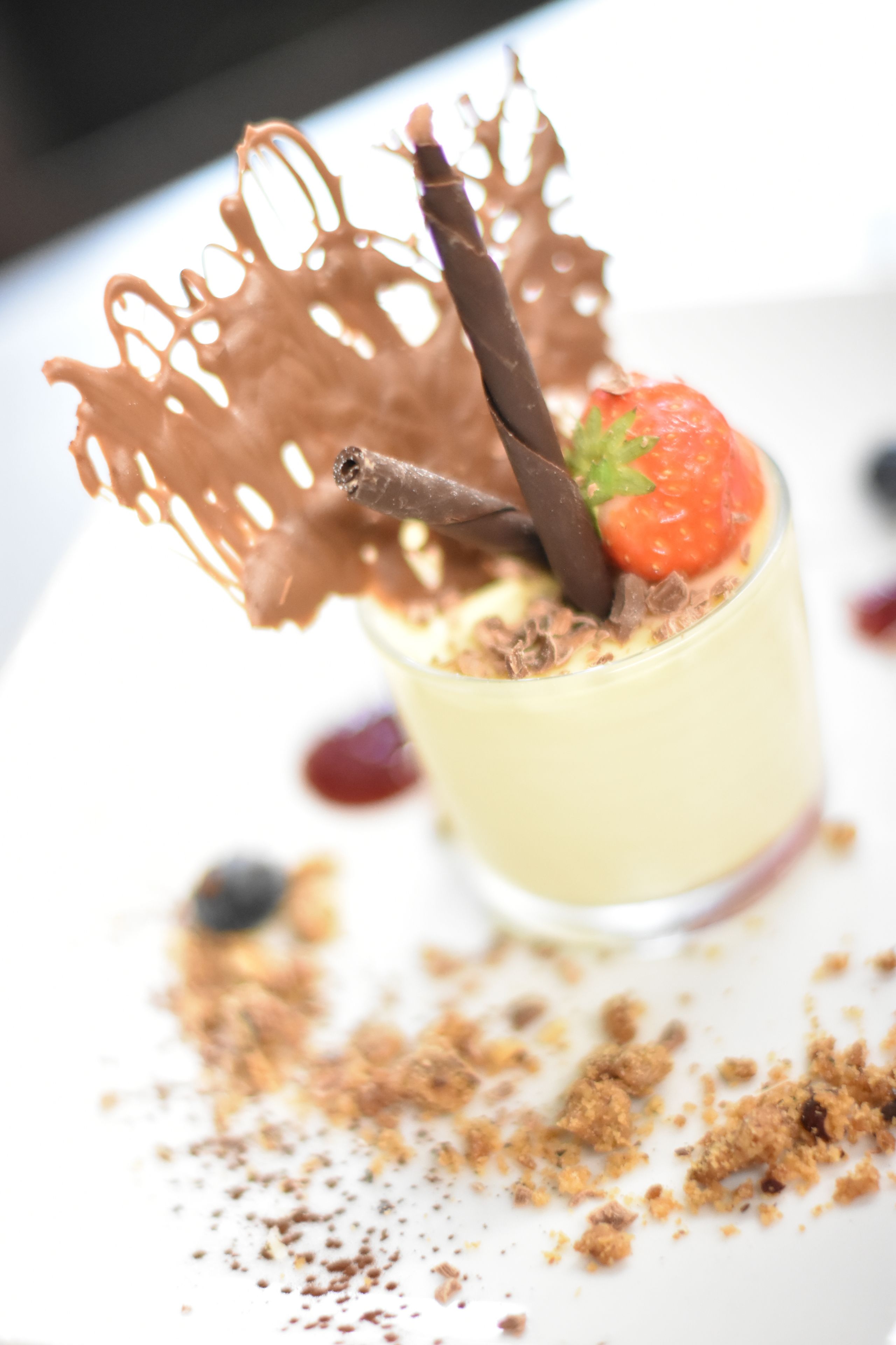 A dessert with a chocolate leaf garnish, a strawberry, and a chocolate stick.
