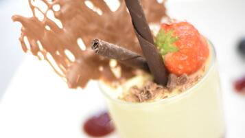 A dessert with a chocolate leaf garnish, a strawberry, and a chocolate stick.
