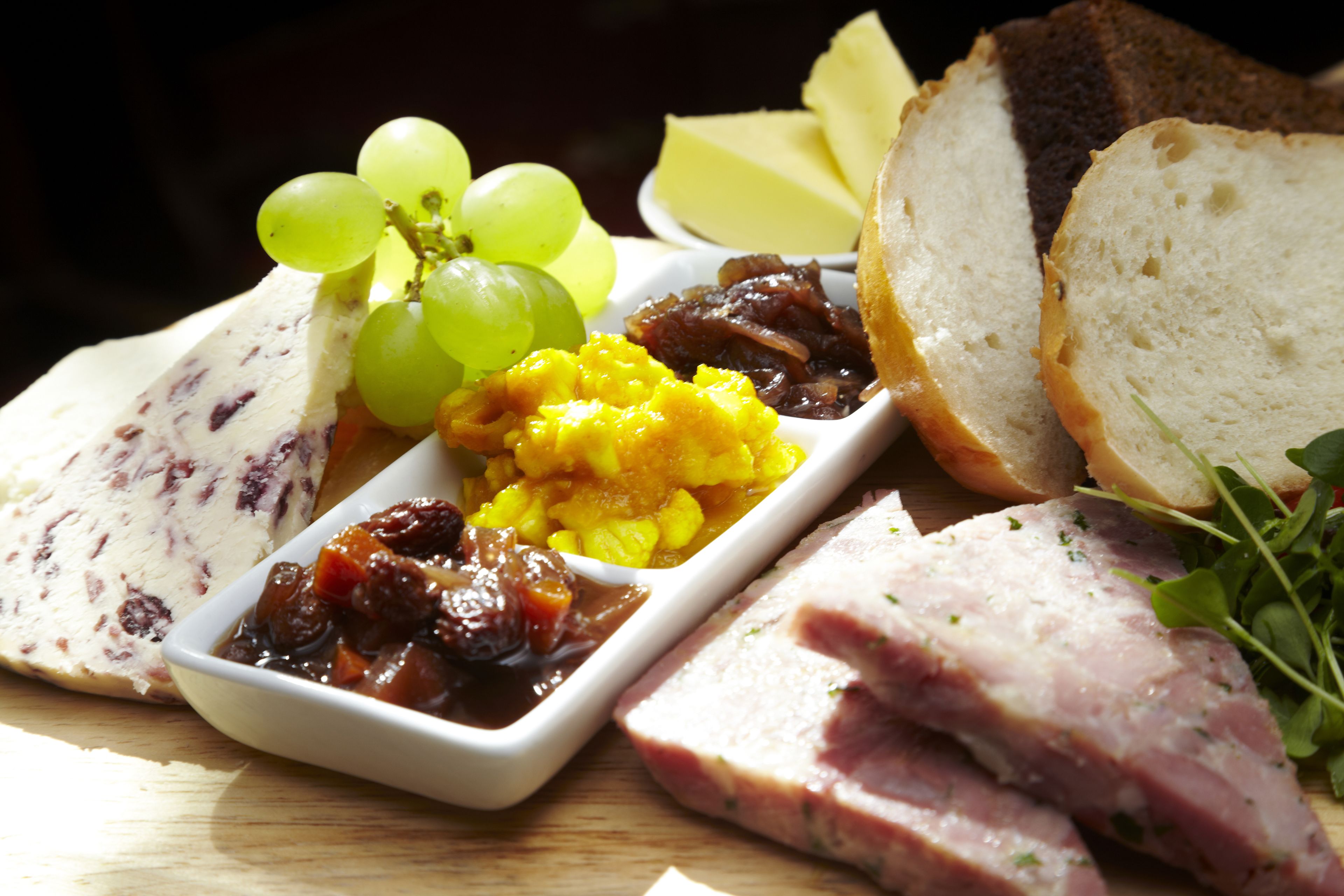 Variedad de alimentos como queso, jamón, uvas y pan sobre una mesa de madera.