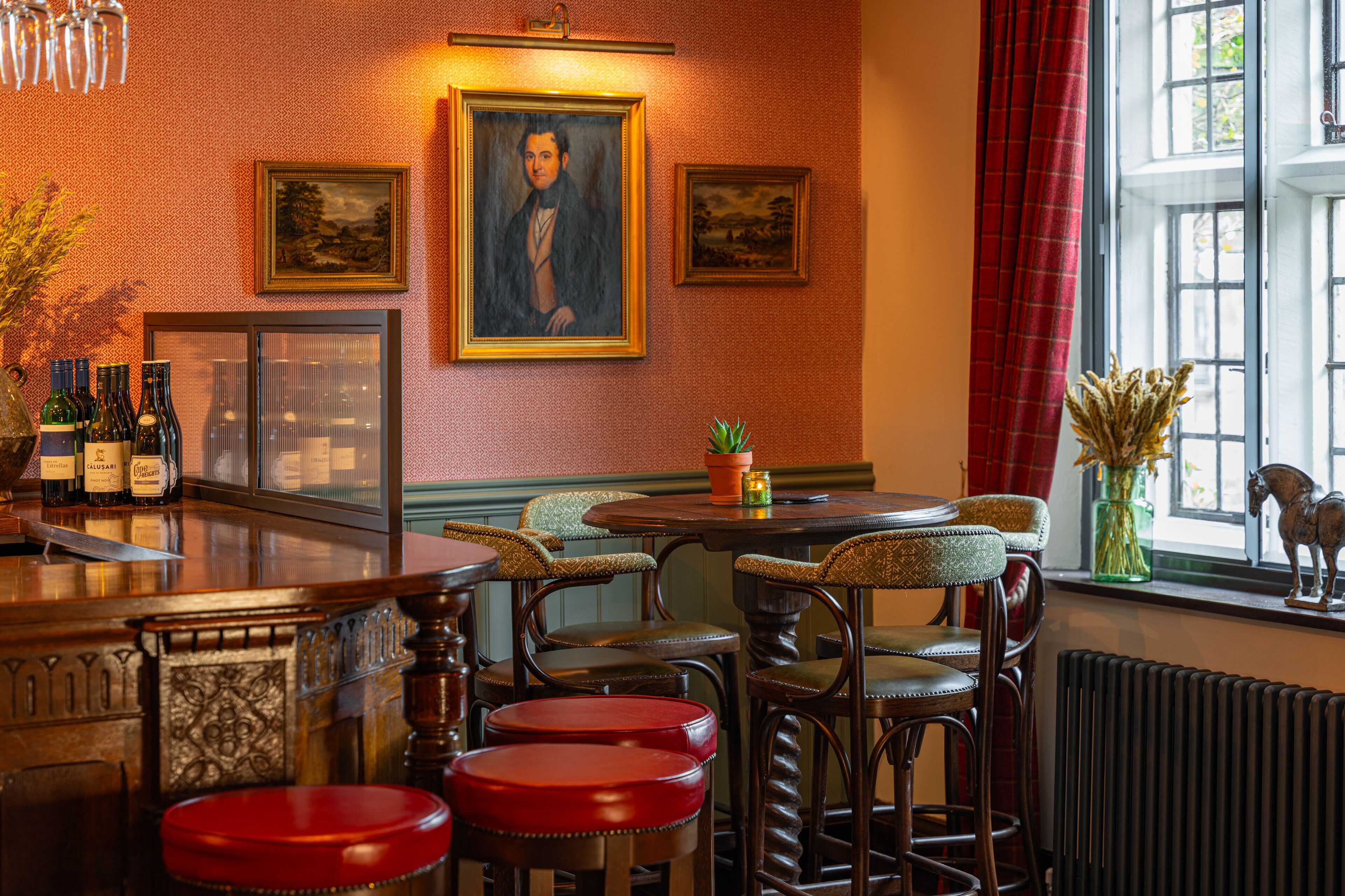 Un área de bar con taburetes de madera, una barra y obras enmarcadas en la pared.